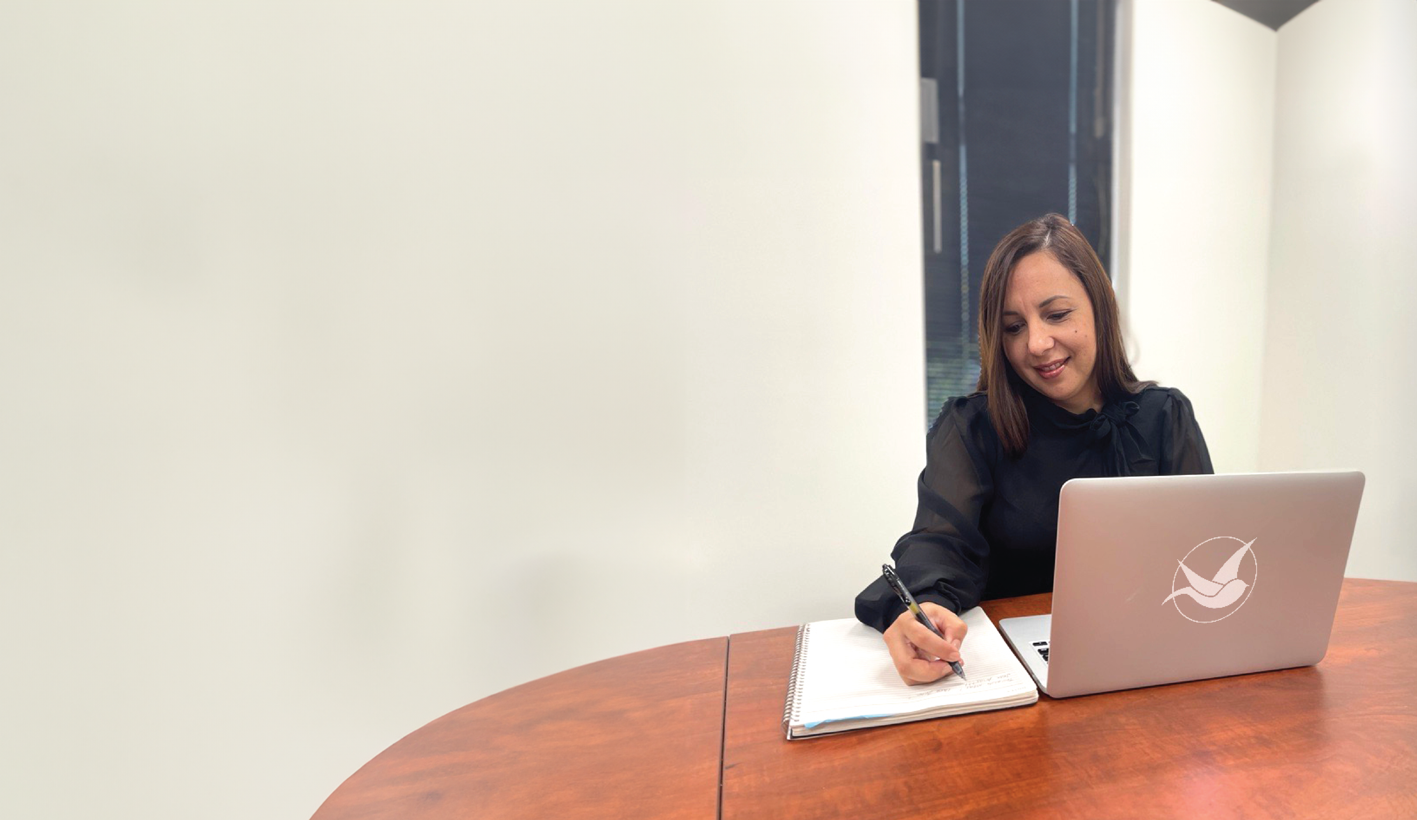 Person writing on a notebook while in front of a laptop