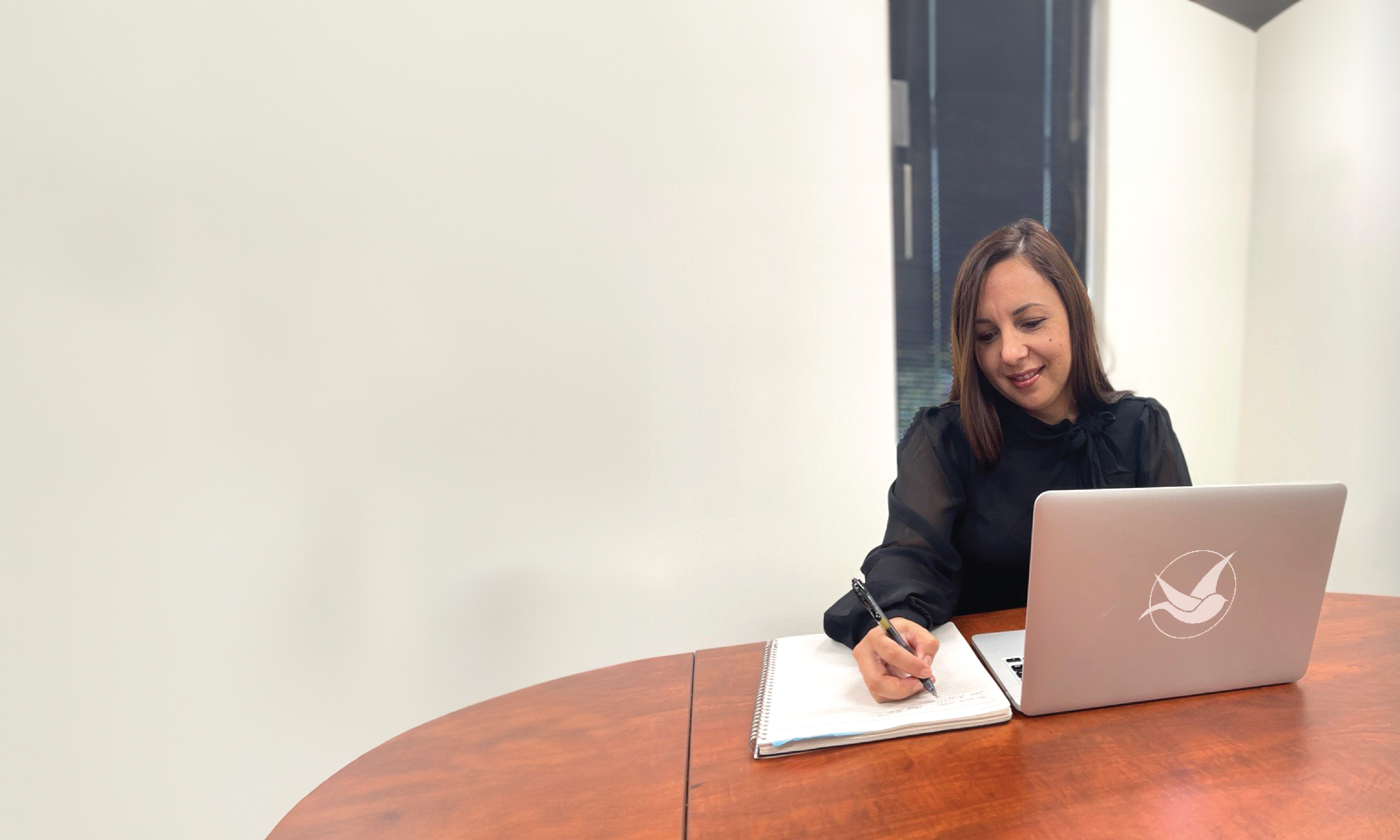 Person writing on a notebook while in front of a laptop